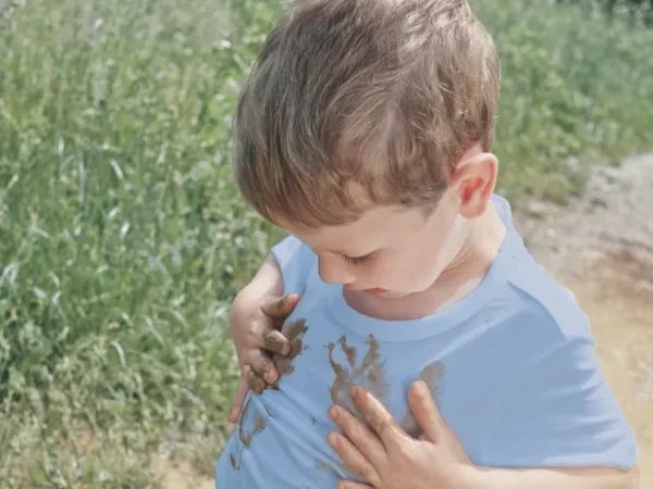 Un bambino che si pulisce le mani sporche di fango sulla camicia