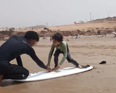 Bambino su una tavola da surf sulla sabbia riceve istruzioni dal suo istruttore durante un campo estivo in Marocco